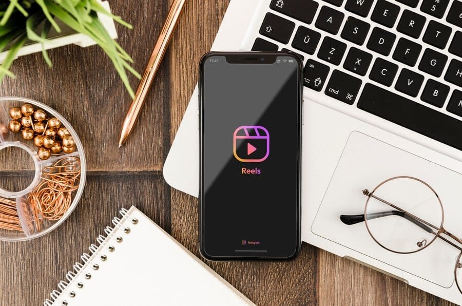 Instagram Reels app displayed on smartphone surrounded by workspace items including keyboard, notebook, and office supplies