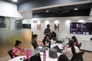 Digital marketing team collaborating in modern office meeting room with video conference setup and laptops