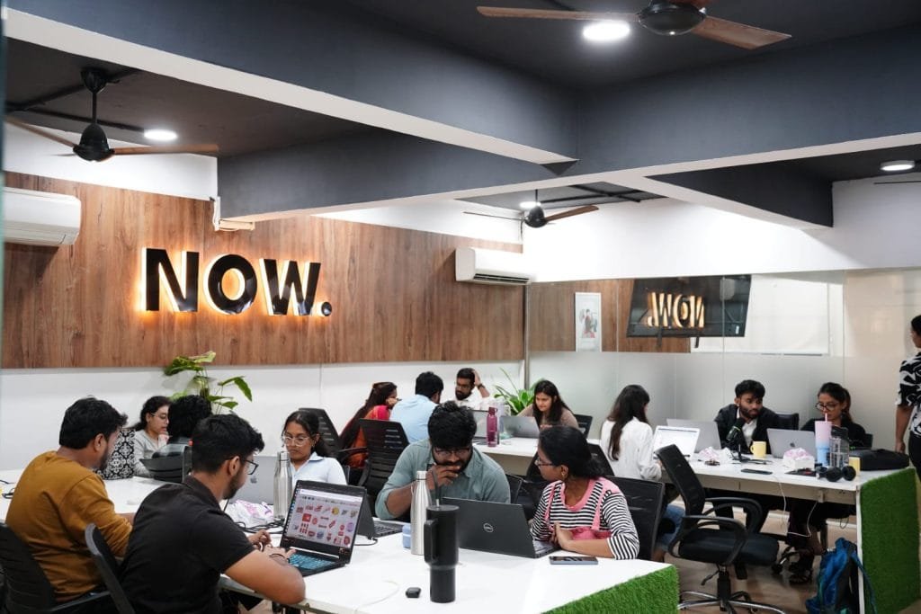 Digital Mojo team collaborating in modern office with laptops and neon NOW sign in Hyderabad