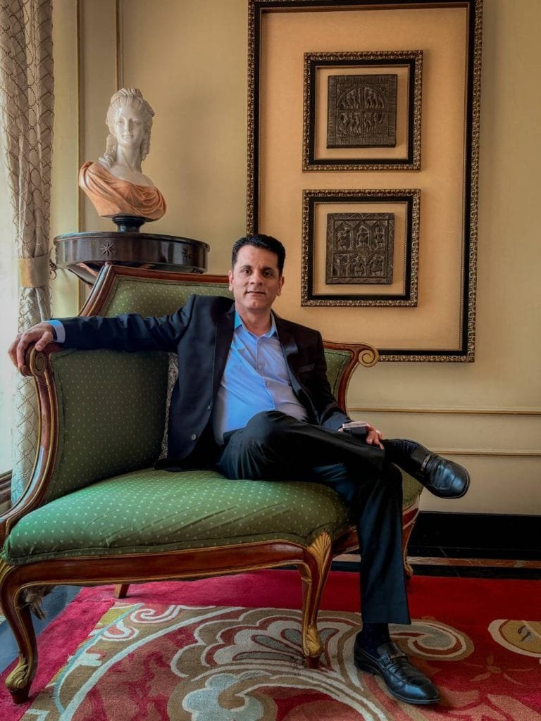 Professional businessman in formal attire relaxing on green velvet settee in luxurious interior with classical art