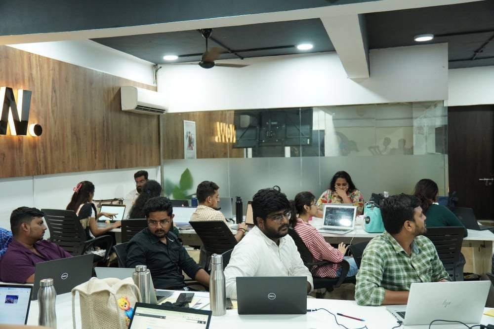 Professional team collaborating in modern office workspace with laptops and multiple workstations
