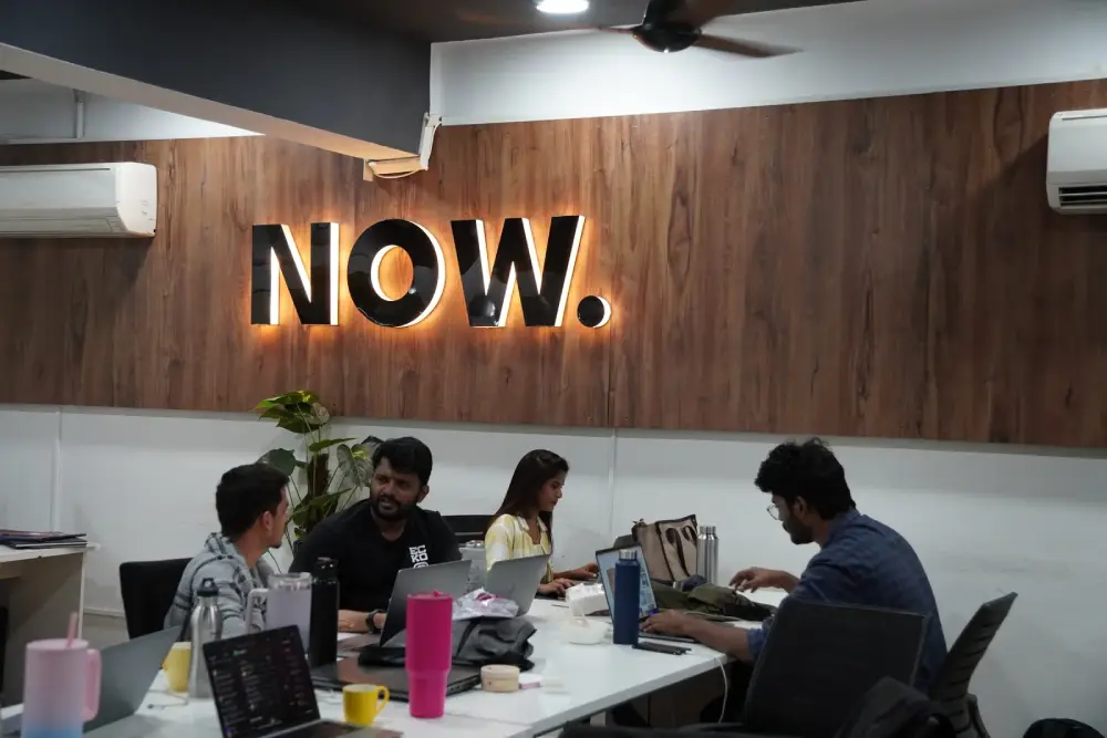 Creative team collaborating at modern office workspace with NOW neon sign at Digital Mojo Hyderabad