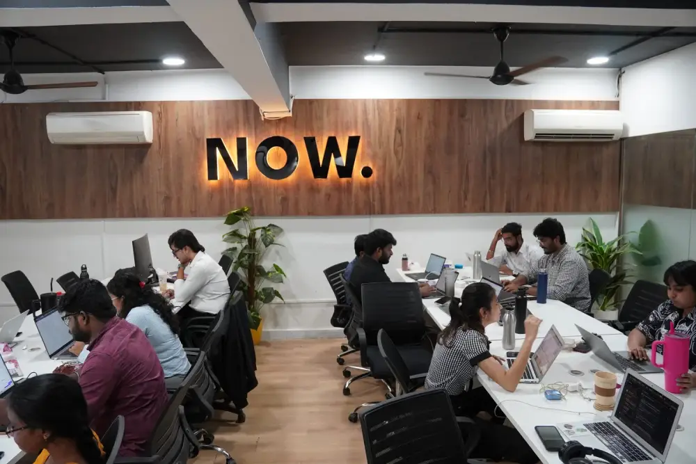 Modern coworking space with diverse team collaborating on laptops under NOW sign in Hyderabad office
