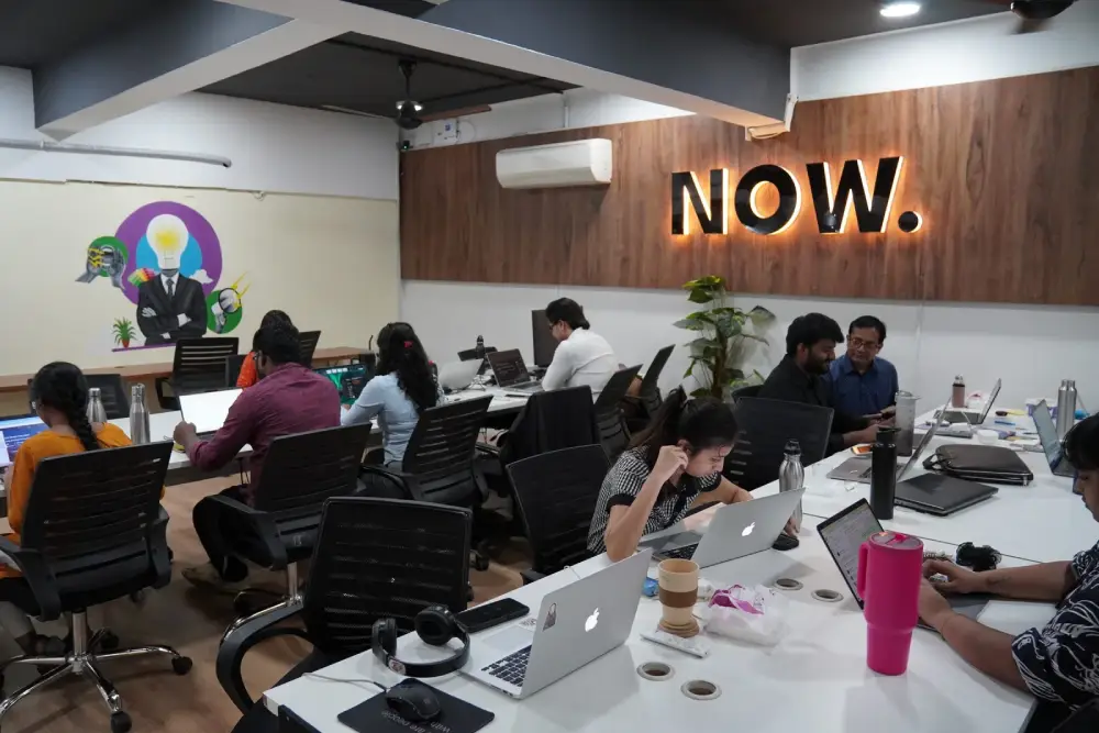 Digital Mojo team collaborating in modern office workspace with laptops and neon NOW sign