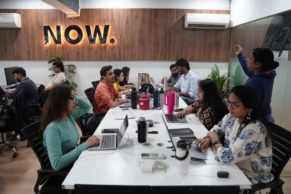 Digital Mojo team collaborating in modern office with NOW sign, laptops and creative workspace setup