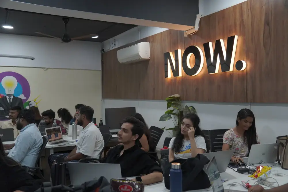 Digital Mojo team collaborating in modern office with NOW neon sign, laptops and creative workspace setup