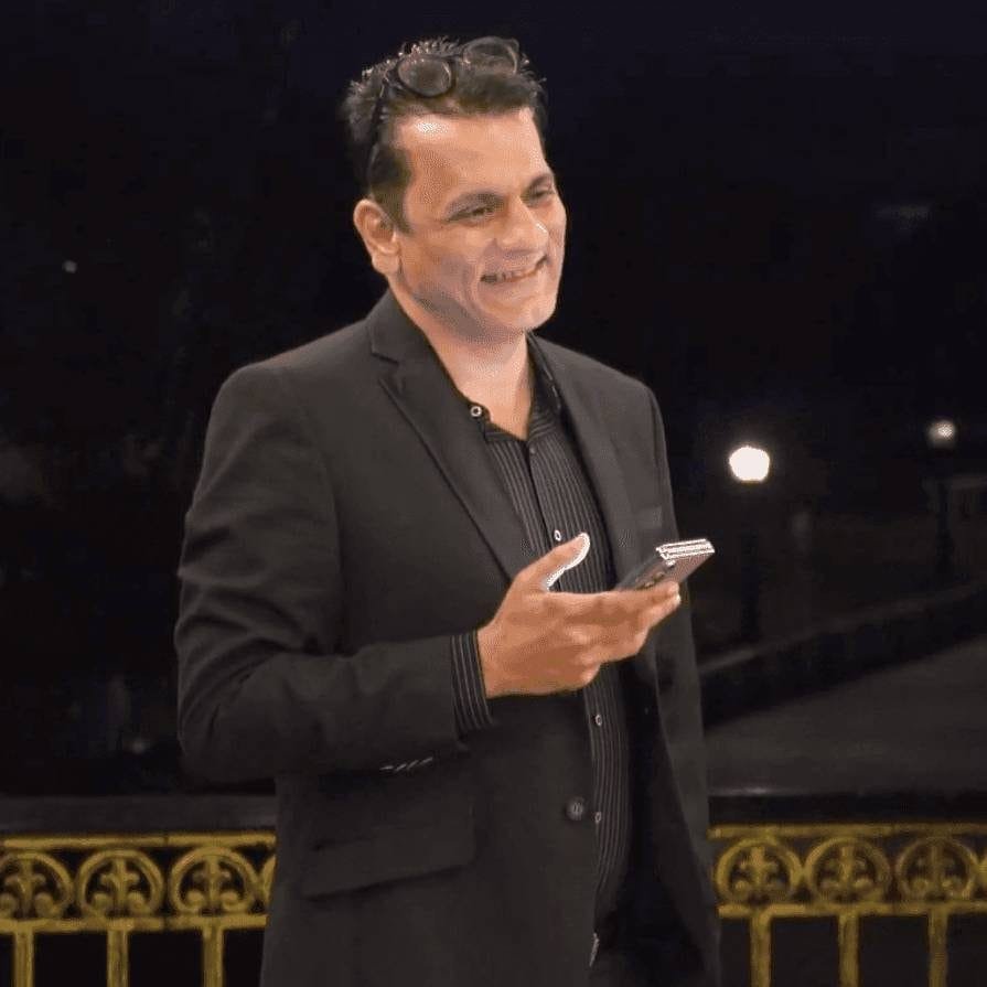 Professional man in black blazer speaking at corporate event with ornate gold railing background